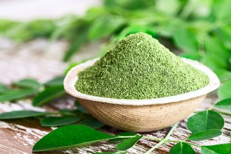 Moringa powder (Moringa Oleifera) in coconut bowl with original fresh Moringa leaves on wooden background. Healthy product, superfood, vitamin.の写真素材