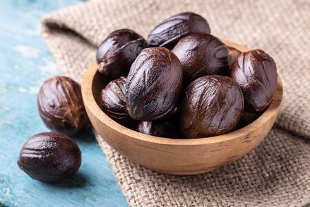 Whole inshell nutmeg nuts in a bowl on the burlap on blue rustic wooden table. Indian spice.の写真素材
