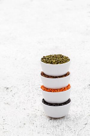 Various assortment set of indian legumes - mung dal, black orid, red masoor dal, horse gram in white melamine bowls on white background with copyspace. Vegetable proteins. Protein products for vegans. Healthy eating concept.の写真素材