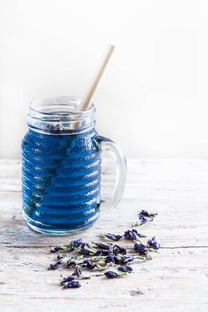 Glass jar of cold  Butterfly pea tea (pea flowers, blue pea) on old rustic table. Healthy detox herbal caffeine free fresh trendy drink.の写真素材