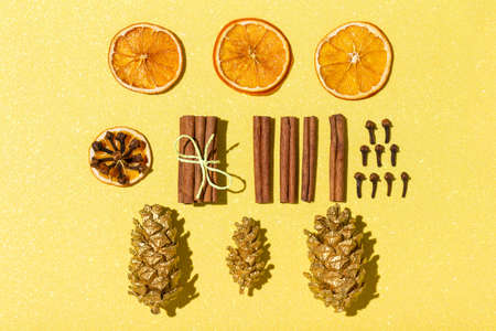 New Year's and Christmas composition on glittering yellow background. Flat lay, top view arrangement of dried orange rings, cinnamon, clove, golden pine cones. Ingredients for mulled wine. Knolling.の写真素材