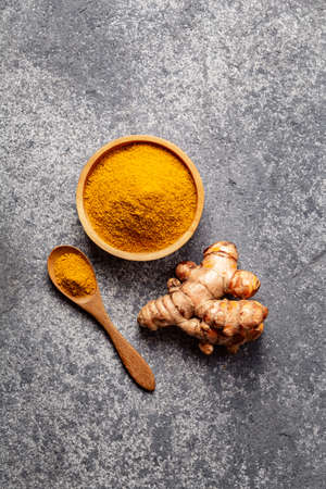 Turmeric powder and fresh turmeric root on gray concrete background. Spice, natural coloring, alternative medicine.の写真素材