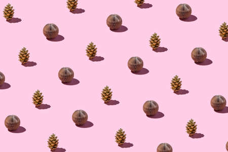 Trendy Christmas and New year pattern made with handmade golden pine cones and paper balls on bright light pink background.の写真素材