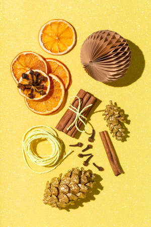 New Year's and Christmas composition on glittering yellow background. Flat lay, top view arrangement of dried orange rings, cinnamon, clove, golden pine cones. Ingredients for mulled wine.の写真素材