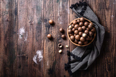 Organic ripe whole Macadamia nuts in bowl on old wooden rustic table top view. Healthy vegan vegetarian food, vitamin.の写真素材