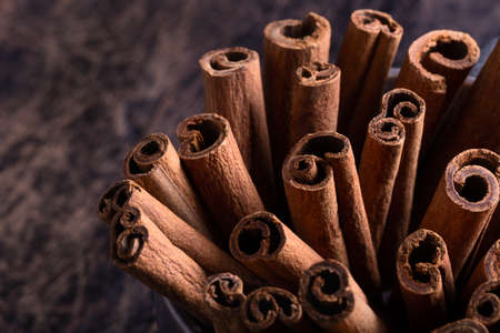 Cinnamon sticks in ceramic bowl on black rustic background with copyspace. Dark photo. Indonesian...