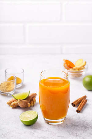 Healthy drink from turmeric and ginger roots and lime in a glass on white concrete background with...