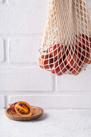 Sliced tamarillo fruit on plate and in eco mesh bag hanging on white wall. Shopping with textile bag. Zero waste concept. tropical summer.の写真素材