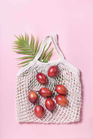 Tamarillo fruit on mesh bag on pink background minimal flat lay. Shopping with textile bag. Zero...