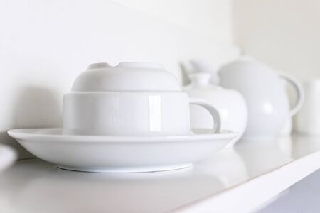 White ceramic coffee cups and saucers standing in a row on a shelf in kitchen.
