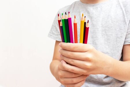 A boy, child holding different colorful pencils of different colors close up on white background,...