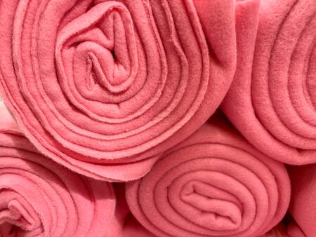 Many rolled up pink colorful fleece blankets close up in a store, home comfort concept.