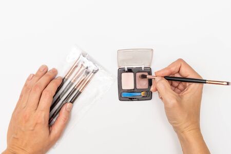 Hands with a brushes for makeup and a palette two brown eyeshadows on a white background.