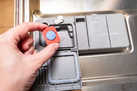 A hand putting a dishwasher tablet into the container of a dishwashing machine.の写真素材