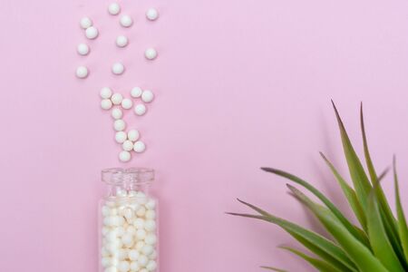 Homeopathic globules scattered from a clear glass bottle on light pink background, alternative homeopathy medicine concept.の写真素材