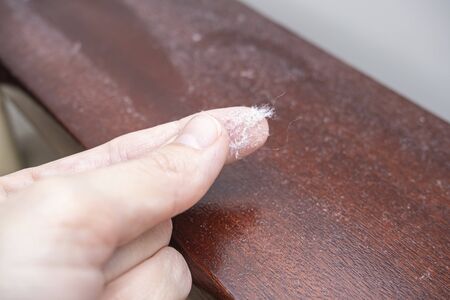 Fingers holding dust from wooden polished surface of furniture, dusty home concept.