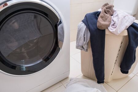 A laundry basket full of dirty laundry on the bathroom floor and washing machine, household concept.の写真素材