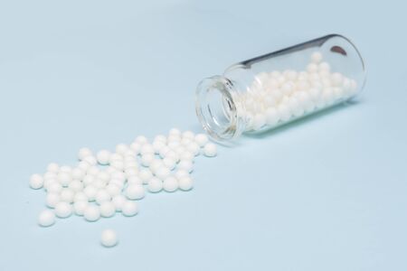 Homeopathic globules scattered from a clear glass bottle on light blue background, alternative...