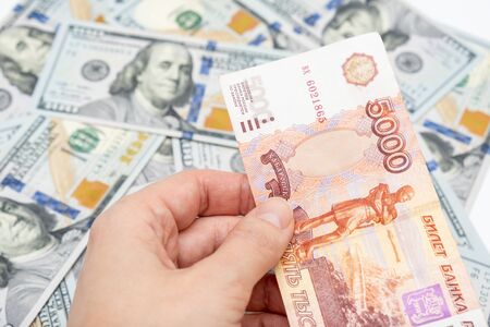 A hand holding 5000 rubles banknote over us dollar background, financial crisis and choosing...