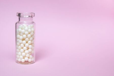 Homeopathic globules in a clear glass bottle on light pink background, alternative homeopathy medicine and naturopathy concept, copy space.の写真素材
