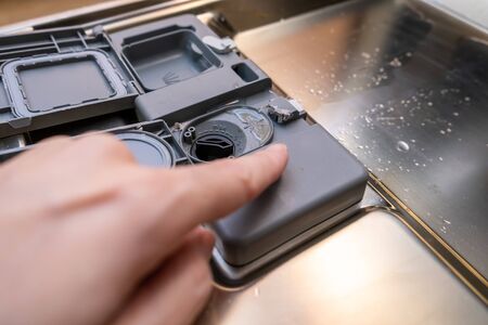 A finger showing on plastic detergent and conditioner dispenser of a dishwasher. Open container, compartment of a dishwashing machine close up.の写真素材