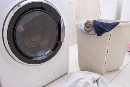 Modern washing machine in a bathroom with a big laundry basket full of dirty linen and clothes.の写真素材