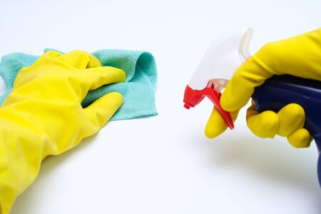 Hands in yellow rubber gloves wiping dust with microfiber cloth and spraying with cleaning agent...