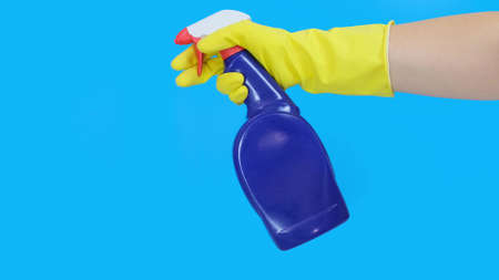 Hand in yellow rubber glove holding a blue cleaning spray bottle close up and using it, blue...