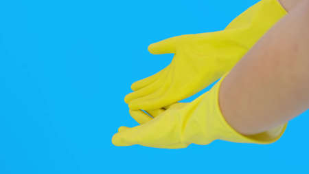 Hands of a woman housewife in yellow protective latex rubber gloves against blue background,...