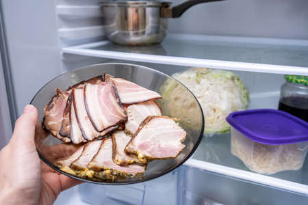 hand putting sliced boiled cooked meat, bacon into the fridge for storage.の写真素材