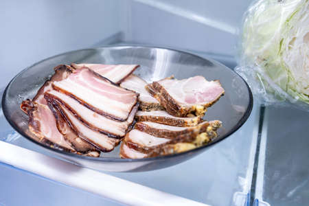A dish with sliced boiled cooked meat, bacon stored on a shelf of a fridge.の写真素材
