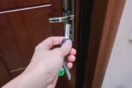 A hand holding a key and inserting it in a keyhole in order to open or lock a door, home security and protection concept.の写真素材