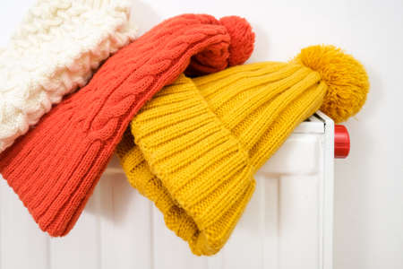 Colorful winter knitted caps, hats hanging and drying on a hot central heating radiator, winter family outdoor activities and sports concept.の写真素材