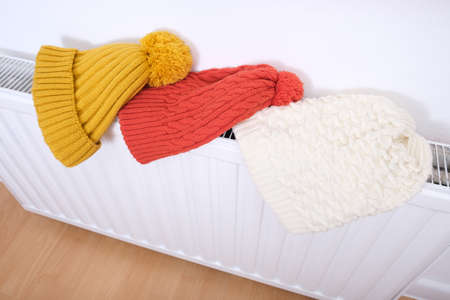 Colorful winter knitted caps, hats hanging and drying on a hot central heating radiator, winter family outdoor activities and sports concept.の写真素材