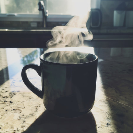 Dark mug of steaming coffee on a sunlit kitchen counterの素材