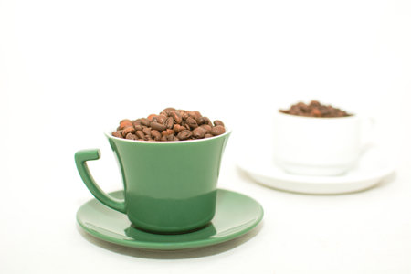 Coffee beans in a green cup and saucer on white backgroundの写真素材