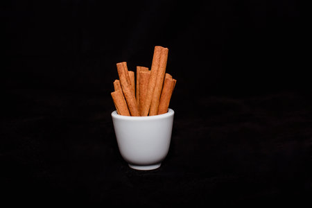 Cinnamon sticks in a white cup on a black background, close upの写真素材