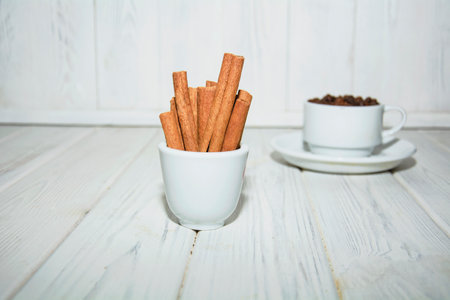 Coffee beans and cinnamon sticks in cup on white wooden backgroundの写真素材