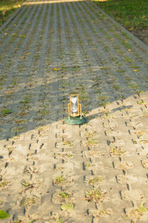 A small hourglass lies on the sidewalk in the park on a sunny day.