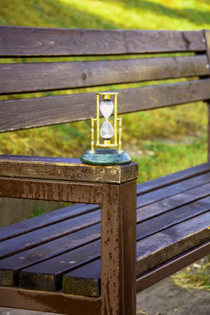 Hourglass on a wooden bench in the park, closeup of photoの写真素材
