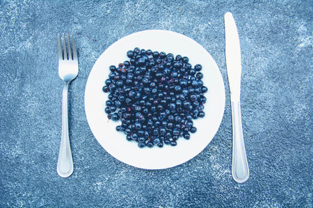 Blueberries in a white plate on a blue background, top viewの写真素材