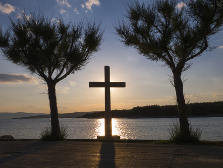 A cross between two trees. Rays of the sun behind a Holy Cross.の写真素材