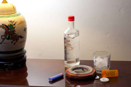 Pills, glass with ice and liquor bottle on coffee table ready to partyの写真素材