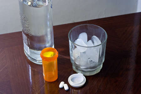 Glass of ice and a liquor bottle with pills and empty bottle.の写真素材