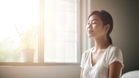 Beautiful asian woman relaxing at home. She is sitting on the windowsill and smiling.の素材