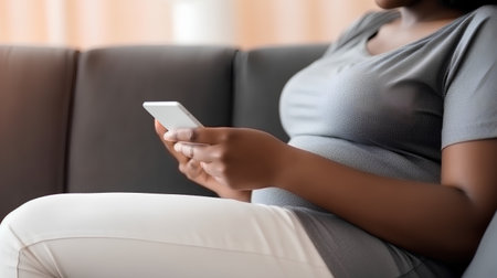 Midsection of pregnant woman using mobile phone while sitting on sofa at homeの素材