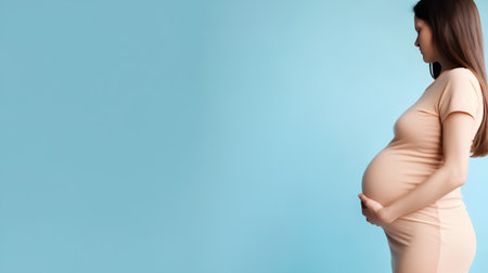 pregnant woman in beige dress on blue background with copy spaceの素材