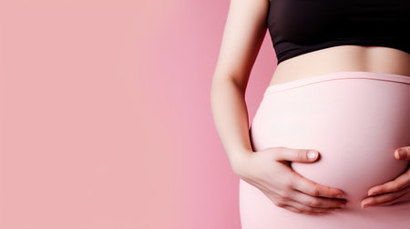 Pregnant woman holding her belly on pink background, closeupの素材
