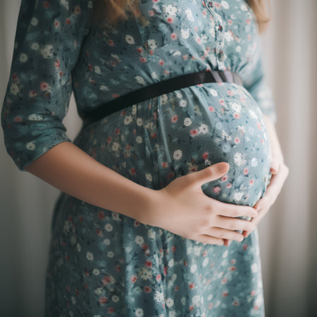 Pregnant woman in blue dress touching her belly with hands.の素材