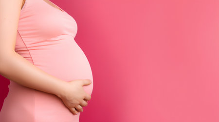 Pregnant woman holding her belly on pink background with copy spaceの素材